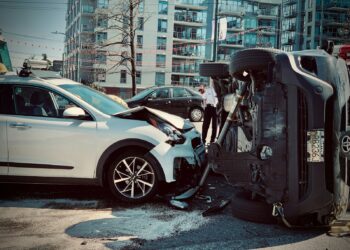 Şehir içinde kazada devrilmiş siyah bir otomobil ve arkasında beyaz araç.