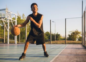 Açık havada basketbol sahasında top süren genç siyah erkek atlet.