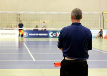 Salonda sırtı dönük duran antrenör veya hakem voleybol sahasına bakıyor.