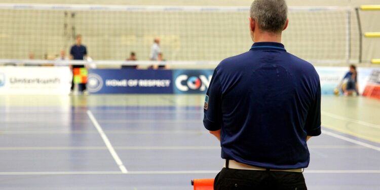 Salonda sırtı dönük duran antrenör veya hakem voleybol sahasına bakıyor.