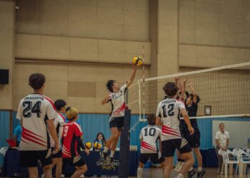 Salonda file önünde smaç vuran voleybolcu ve file üstünde elleriyle blok yapan oyuncular