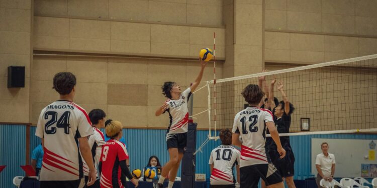 Salonda file önünde smaç vuran voleybolcu ve file üstünde elleriyle blok yapan oyuncular