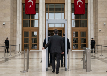 Bir binanın girişinde güvenlik kontrol noktasından geçen insanlar ve görevliler.