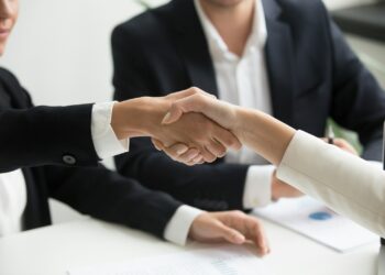 Ofis ortamında birbirleriyle el sıkışan iki iş insanının yakın plan görüntüsü.