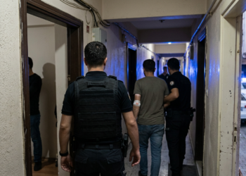 Polis memurları binadaki bir daireden şüpheli bir kişiyi koridor boyunca dışarı çıkarıyor.