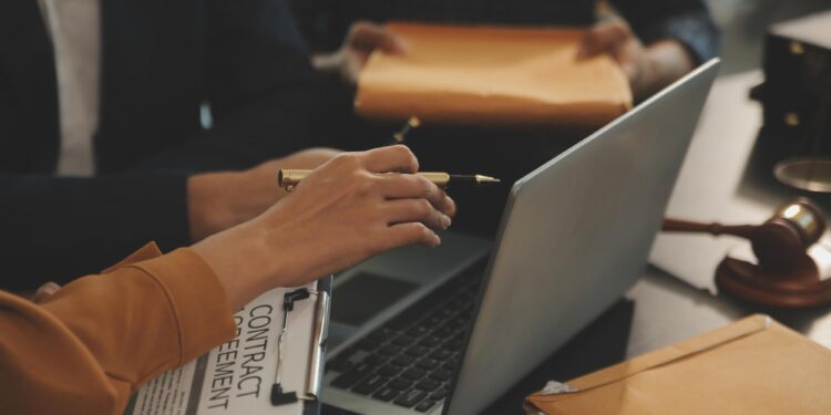Masada çalışan avukat, laptop ve sözleşme evrakları ile hukuki belgeler.