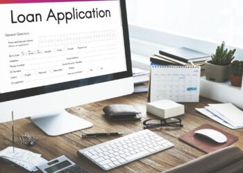Ahşap masada açık loan application yazılı bilgisayar ekranı ve ofis malzemeleri.
