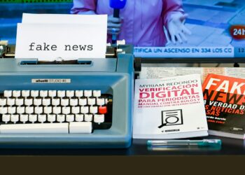 Üzerinde fake news yazan daktilo ve arkasında haber kanalı açık televizyon.