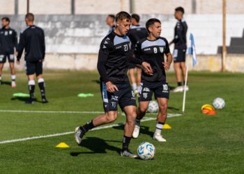 Saha kenarındaki yeşil çimlerde futbol antrenmanı yapan siyah formalı oyuncular