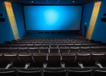 Boş sinema salonu, arkadan ön koltuklara doğru mavi ekranlı büyük perde.
