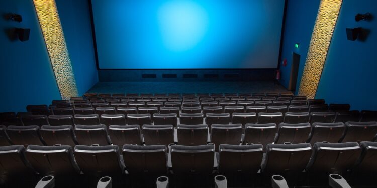 Boş sinema salonu, arkadan ön koltuklara doğru mavi ekranlı büyük perde.