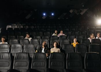 Karanlık bir sinema salonunda koltuklarında oturan ve ekrana bakan seyirciler.