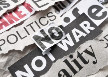 Üzerinde 'No War' ve 'Politics' yazan kırpılmış gazete kupürleri ve küpür yığınları.