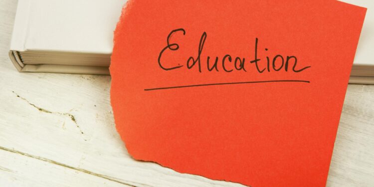 Ahşap zemin üzerinde beyaz kitap ve üzerinde 'Education' yazan kırmızı not kağıdı.