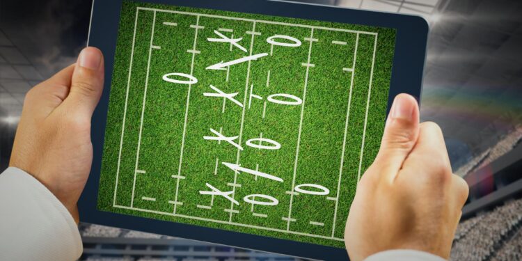 Tablet ekranında futbol taktiği ve oyun şeması gösteren eller.