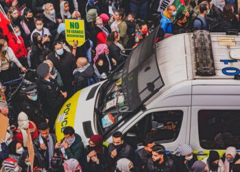 Filistin bayraklı protestocular ve üzerinde polis yazan beyaz bir minibüs.