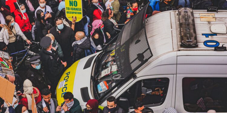 Filistin bayraklı protestocular ve üzerinde polis yazan beyaz bir minibüs.