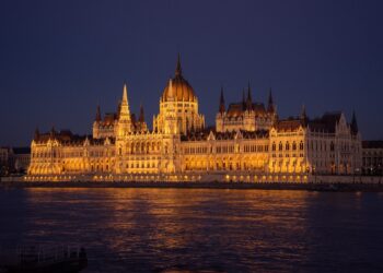 Gece vakti ışıklandırılmış tarihi Macaristan Parlamento Binası ve önündeki Tuna Nehri.